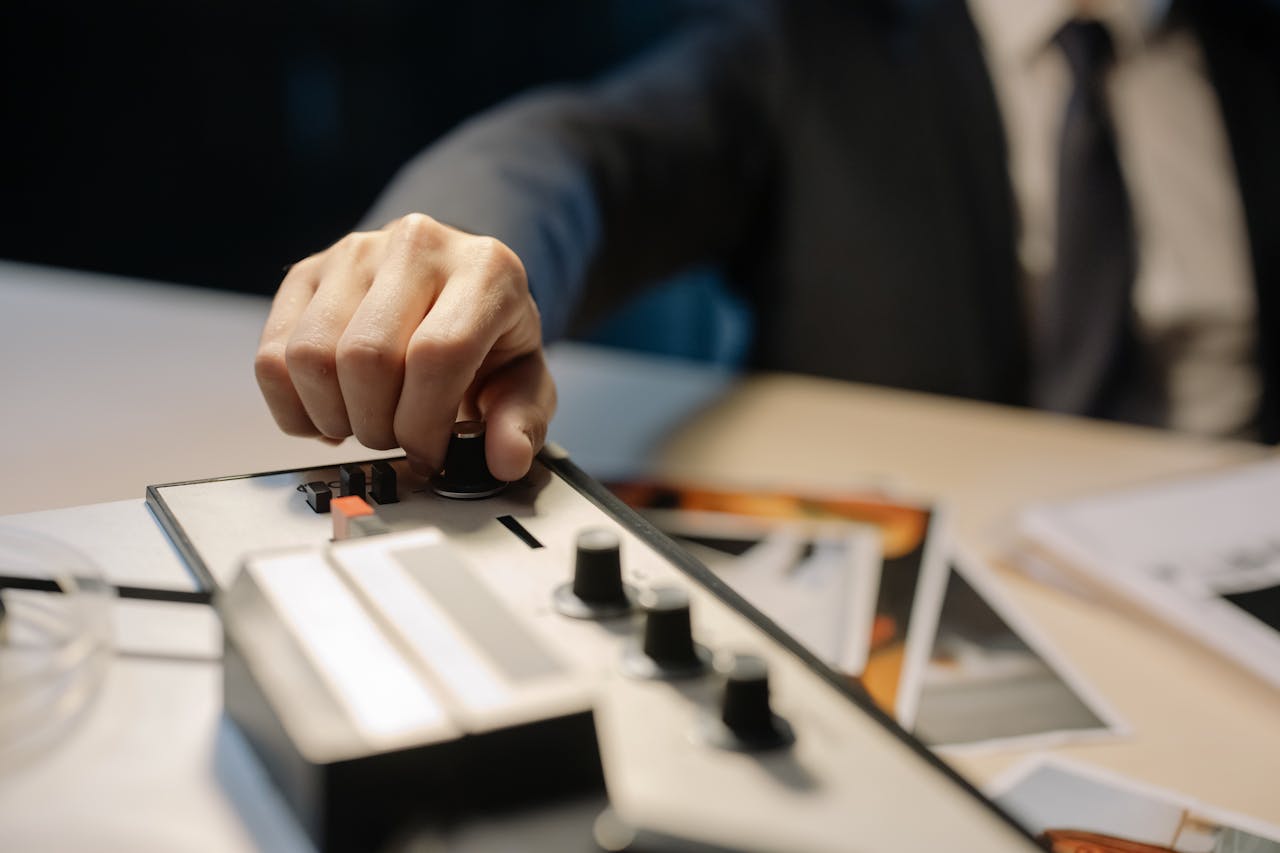A detective's hand adjusts knobs on a vintage tape recorder, suggesting investigation or espionage.